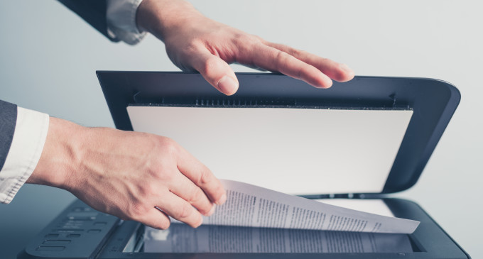 The hands of a young businessman is placeing a document on a flatbed scanner in preperation for copying it